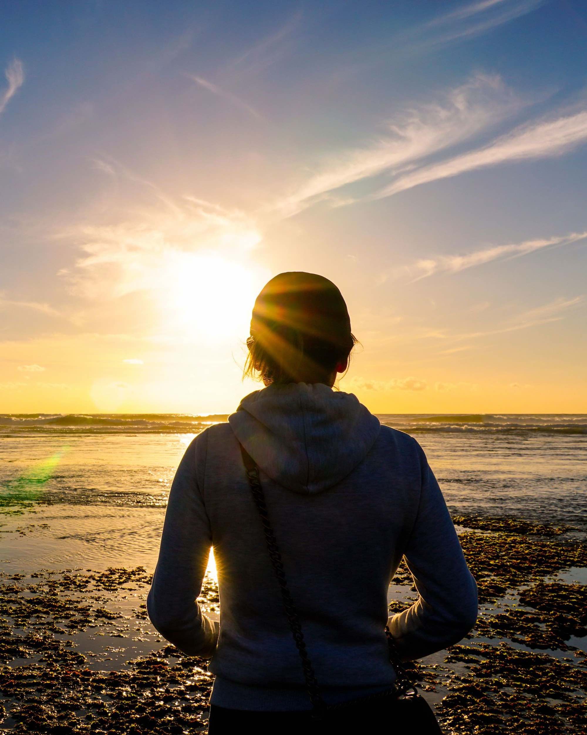 Person standing at the shoreline, looking out at the ocean during golden hour