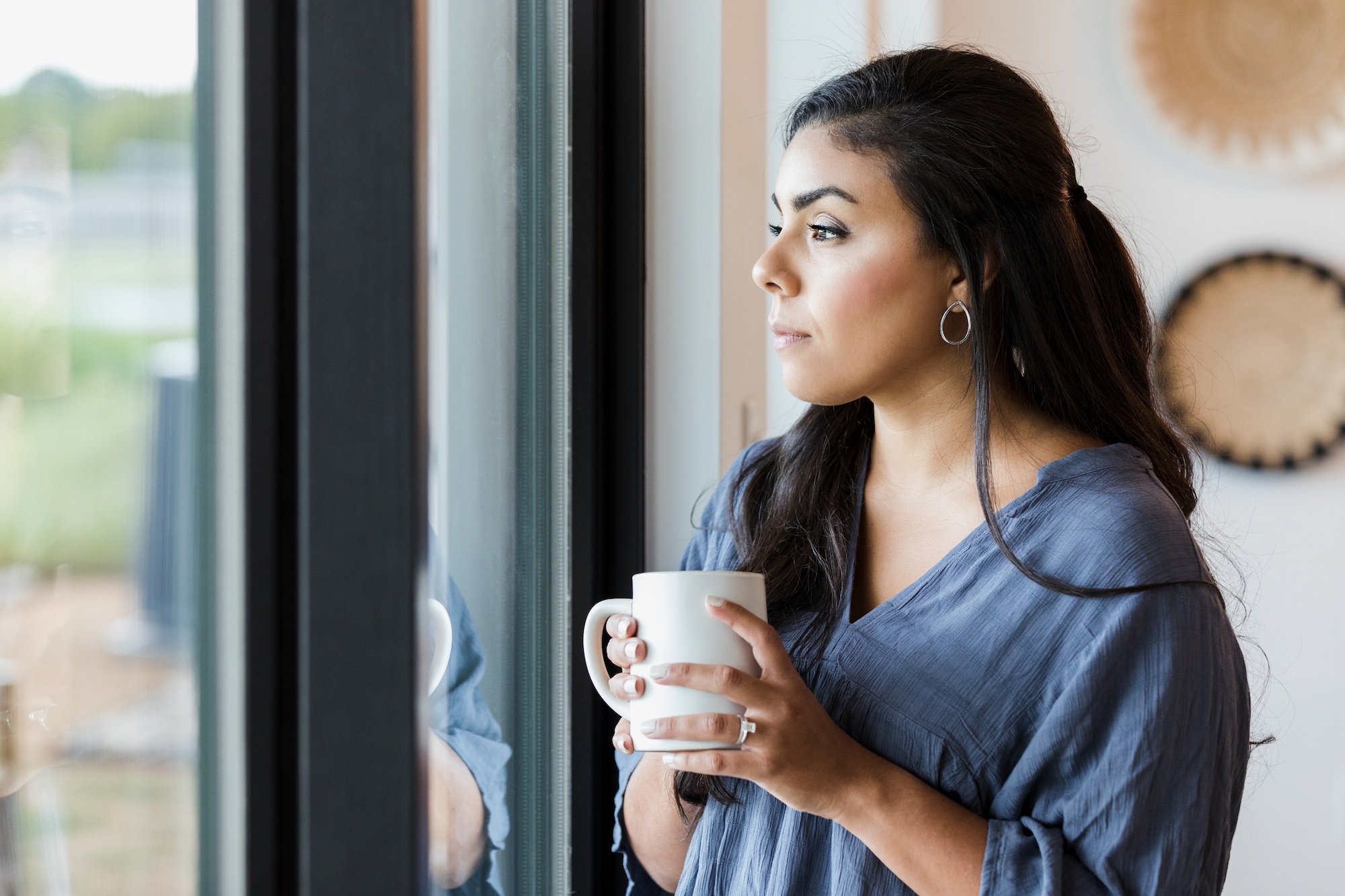Person holding a mug and looking out a window, reflecting quietly while feeling emotionally exhausted